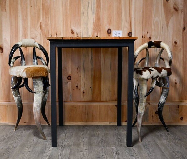 Two chairs with antler backs and a table in front of a wooden wall.