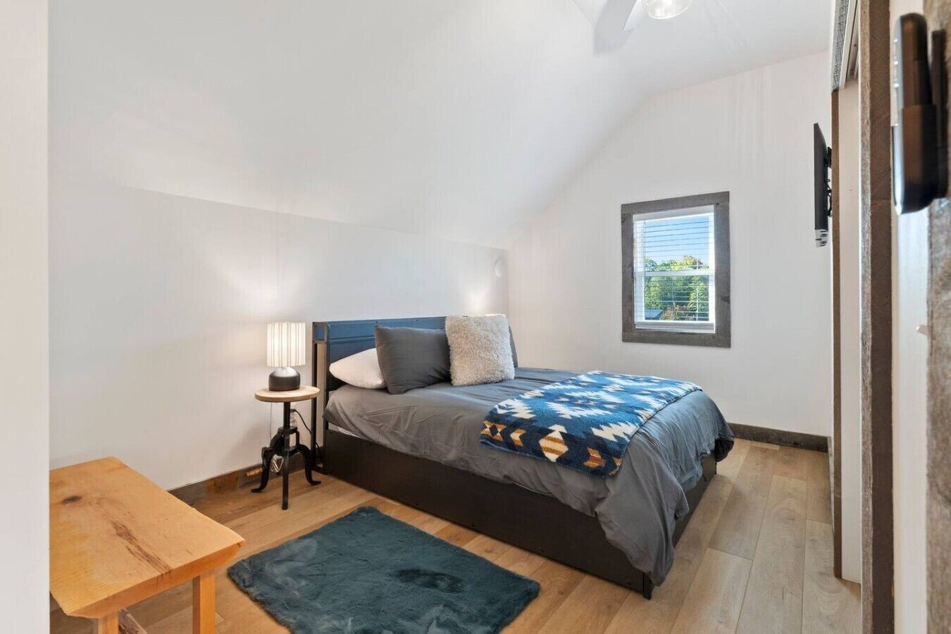Ein Schlafzimmer mit Bett, Nachttisch, Lampe und einem Fenster mit Jalousien.