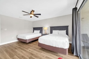 Et hotelværelse med to senge, en ventilator i loftet, et natbord med lampe og udsigt ud.