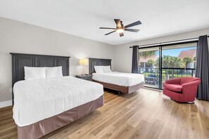 Ein Hotelzimmer mit zwei Betten, einem Deckenventilator, einem roten Sessel und einem Balkon mit Blick.