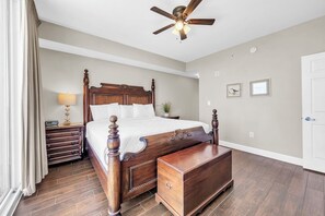Ein Schlafzimmer mit einem hölzernen Bett, einem Nachttisch, einer Kommode, einem Deckenventilator und einer Tür.