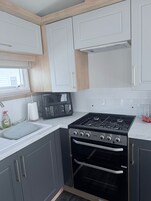 Cocina compacta con estufa a gas, horno y ventana con persianas.
