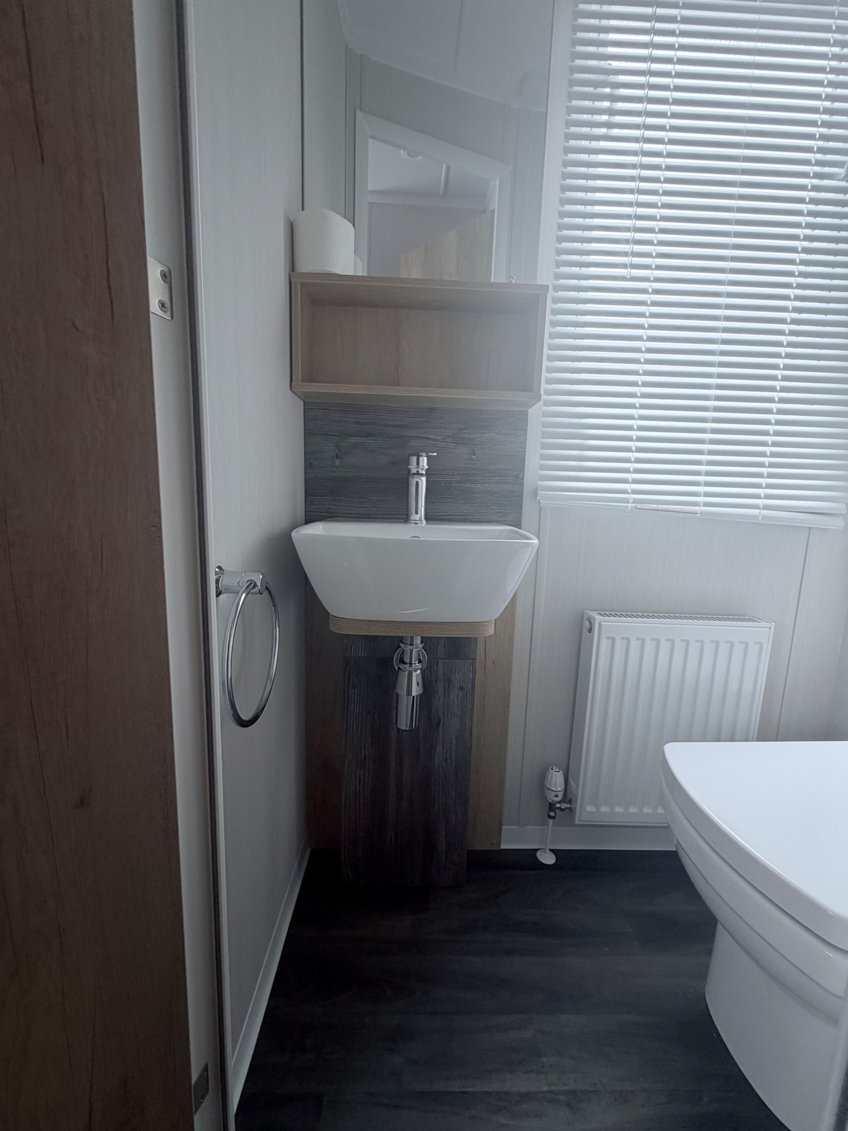 Un baño con lavamanos blanco, inodoro y ventana con persianas.