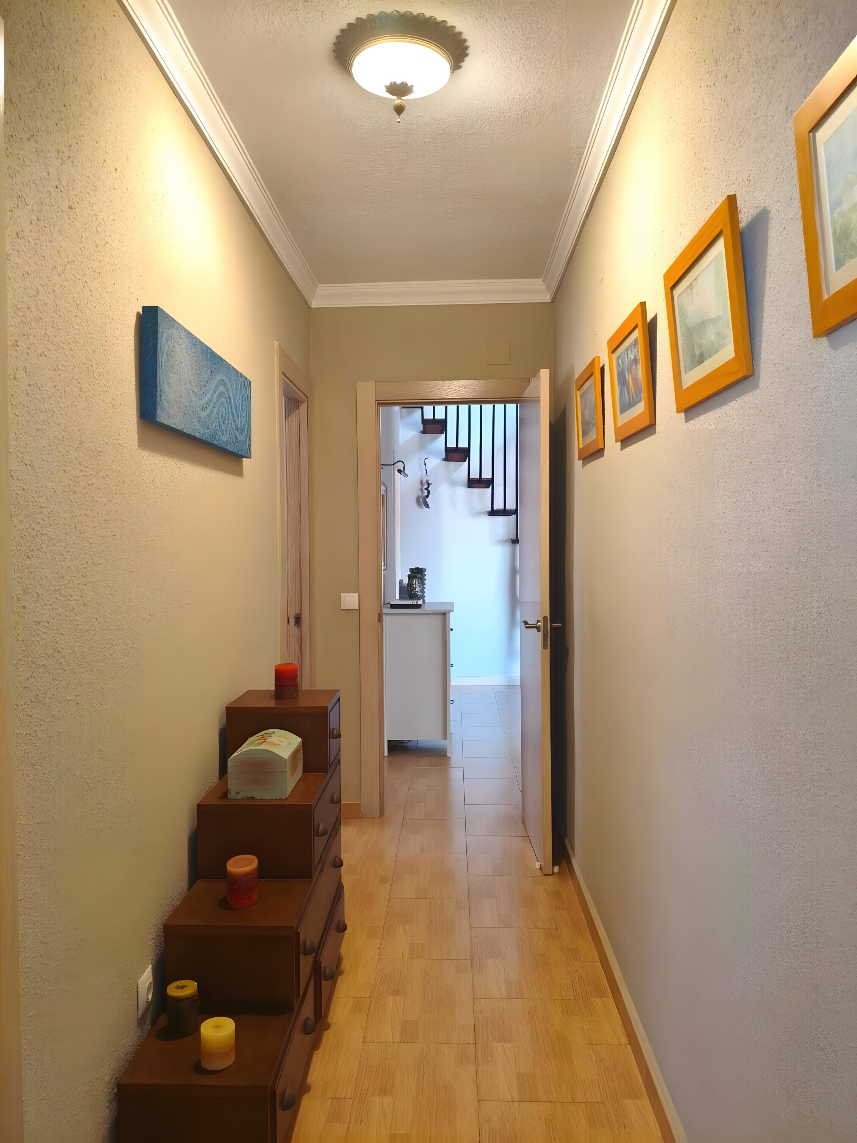Un pasillo con una escalera, armarios de madera y cuadros en las paredes.