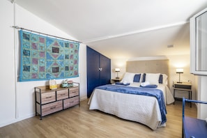 Um quarto com uma cama, cômoda, mesa de cabeceira, luminária e um objeto decorativo na parede.