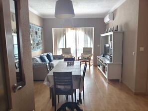 Ein Essbereich mit Tisch, Stühlen und einer Couch. Eine Fernseherin steht auf einem Schrank rechts.