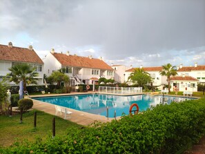 A swimming pool surrounded by white buildings with red-tiled roofs, palm trees, and a clear sky. - Balcón Pueblo Andaluz Apartment with Sea Views, Wi-Fi and Air Conditioning (Torrox)