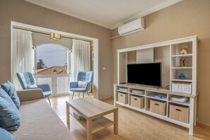 A living room with a sofa, two armchairs, a coffee table, a TV on a wooden stand, and a balcony with curtains. - Balcón Pueblo Andaluz Apartment with Sea Views, Wi-Fi and Air Conditioning (Torrox)