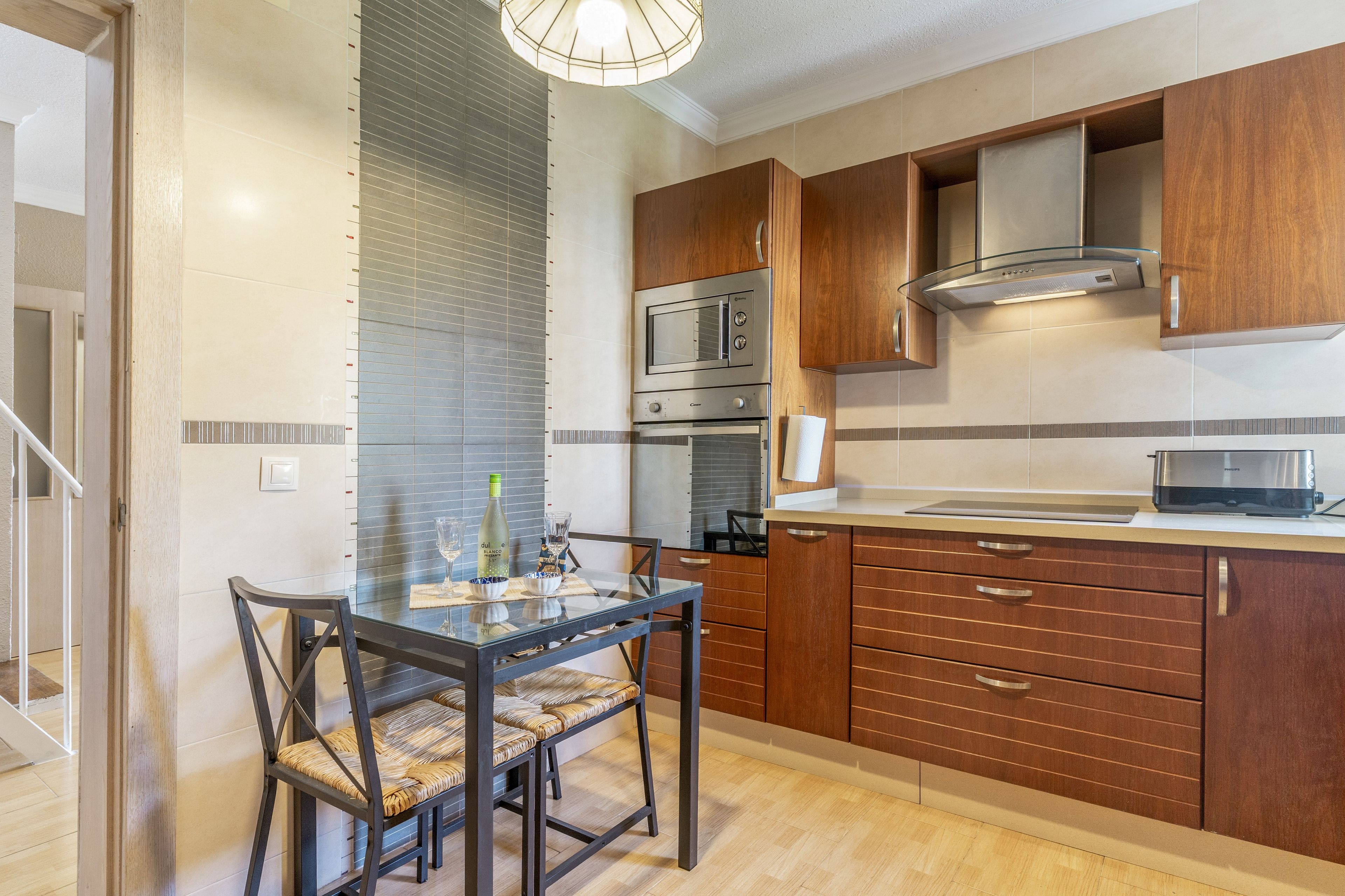 A modern kitchen with wooden cabinets, a glass dining table, and a built-in microwave.
