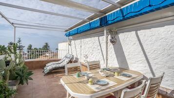 Eine Terrassengaststätte mit Esstisch, gepolstertem Stuhl und Blick aufs Meer.