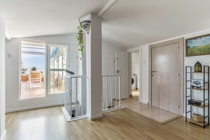 Un amplio salón con suelo de madera, una puerta blanca y vistas al exterior.