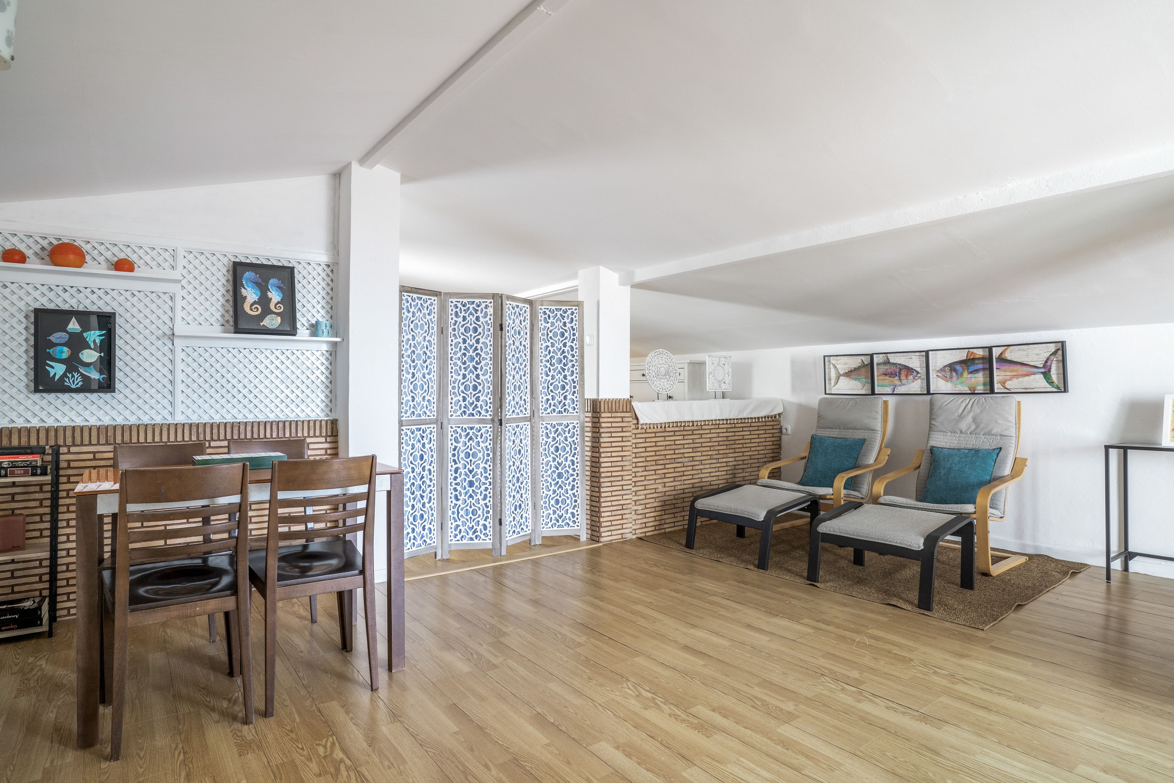 A spacious living area with a wooden floor, a dining set, and a seating area with chairs and a sofa.