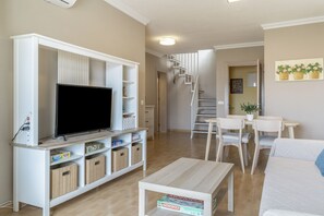 A living room with a flat-screen TV, wooden cabinets, a coffee table, and a staircase leading to another level. - Balcón Pueblo Andaluz Apartment with Sea Views, Wi-Fi and Air Conditioning (Torrox)