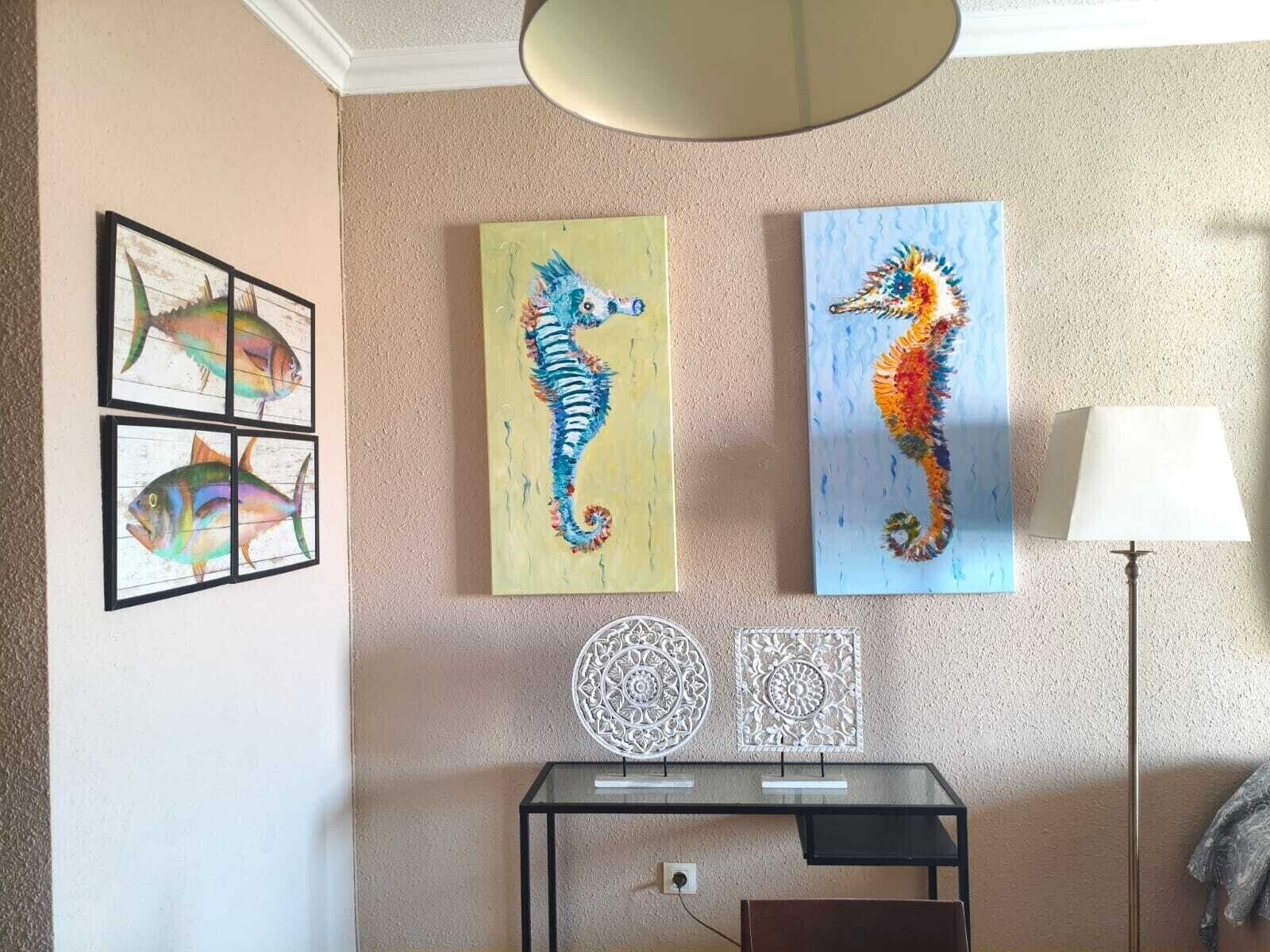 Una habitación con un escritorio, dos cuadros de caballitos de mar y una lámpara.
