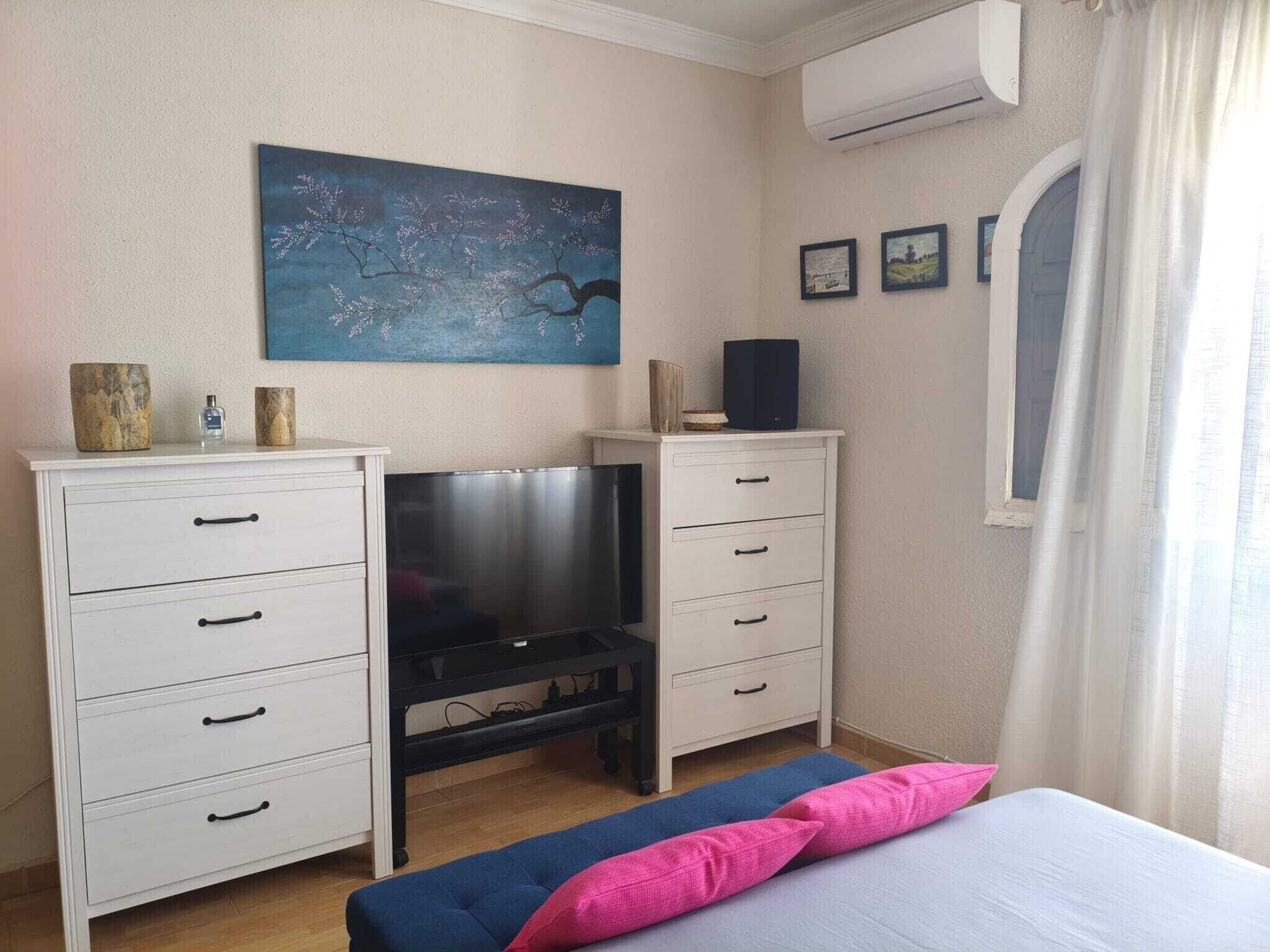 A bedroom with a bed, a TV, two dressers, and a painting on the wall.