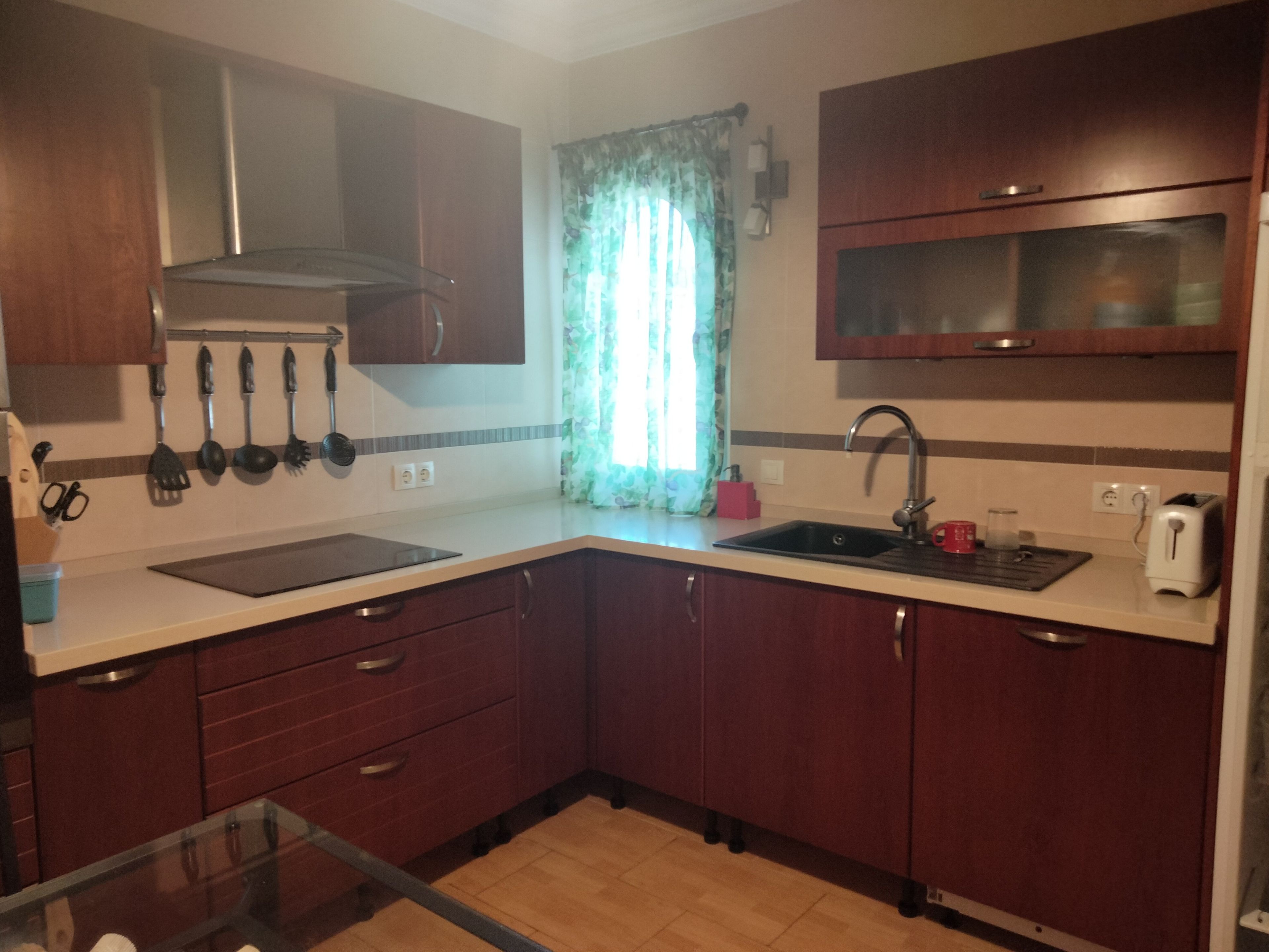 Una cocina con armarios de madera, un lavamanos de acero inoxidable y una ventana con cortinas.
