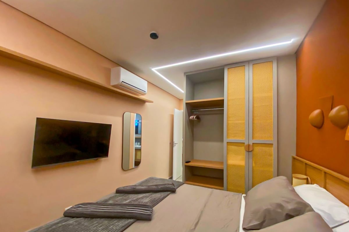 A modern hotel room with a bed, a TV, a wardrobe, and a shower area.