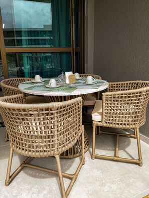 A round table with four wicker chairs, a glass-top table, and a set of white cups and saucers. - Beach Class Solare por YOLO (Ipojuca)