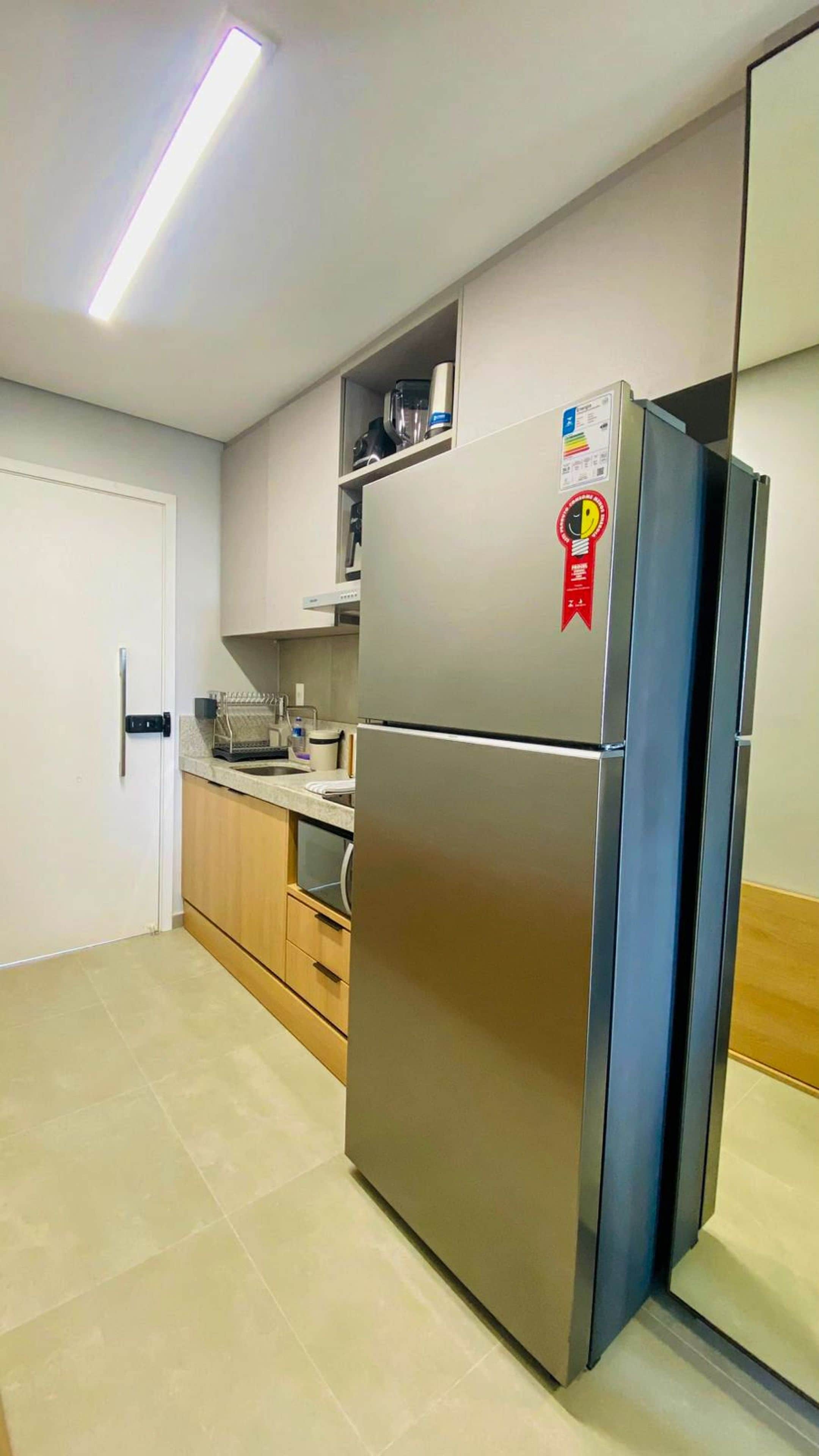 Uma cozinha com geladeira de aço inoxidável, porta branca e bancada com pia.