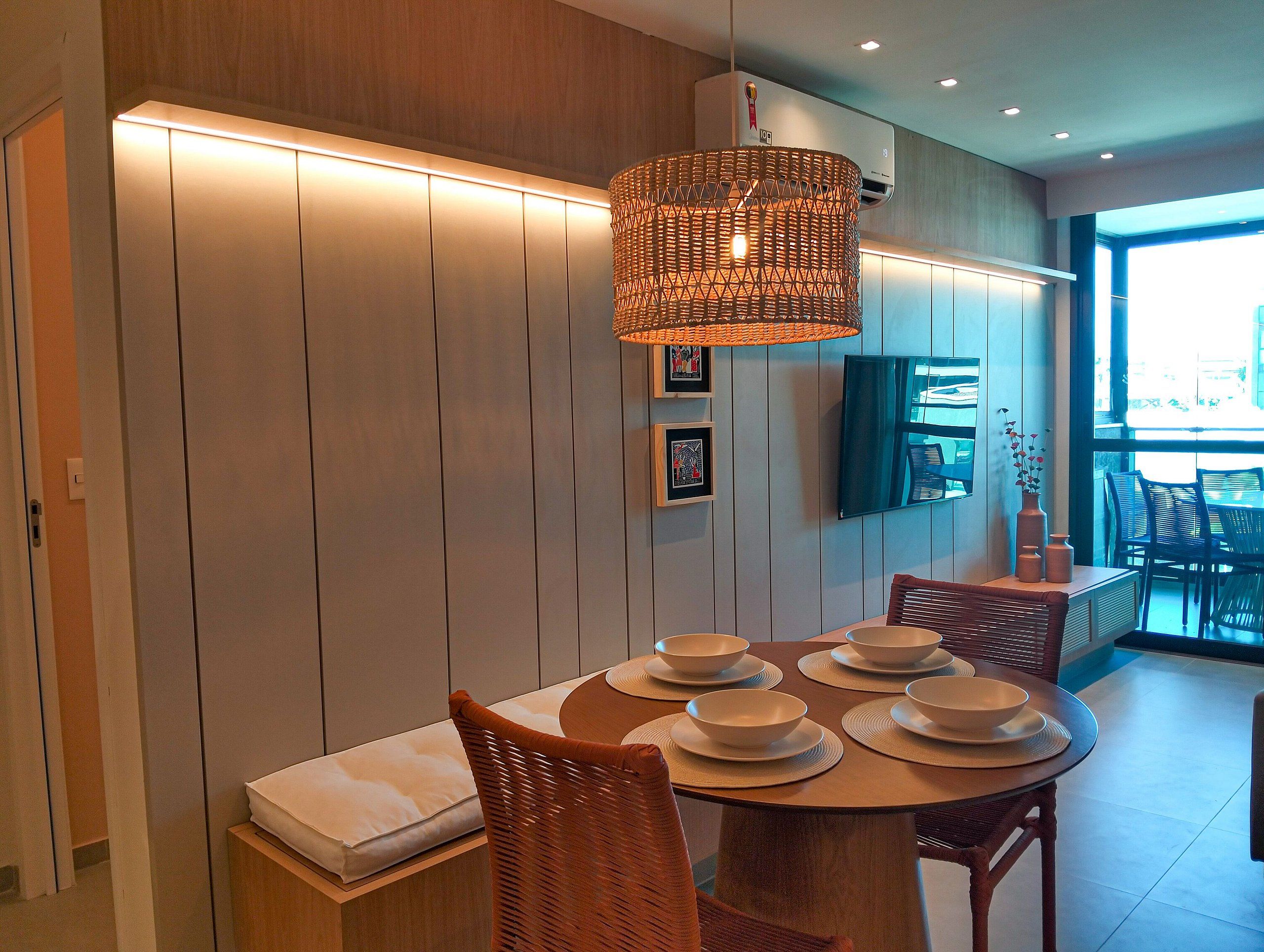 A dining area with a round table set with bowls and plates, a wicker pendant light, and a television mounted on the wall.