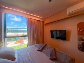 Quarto de hotel com cama, televisão, janela com cortinas e ar condicionado.