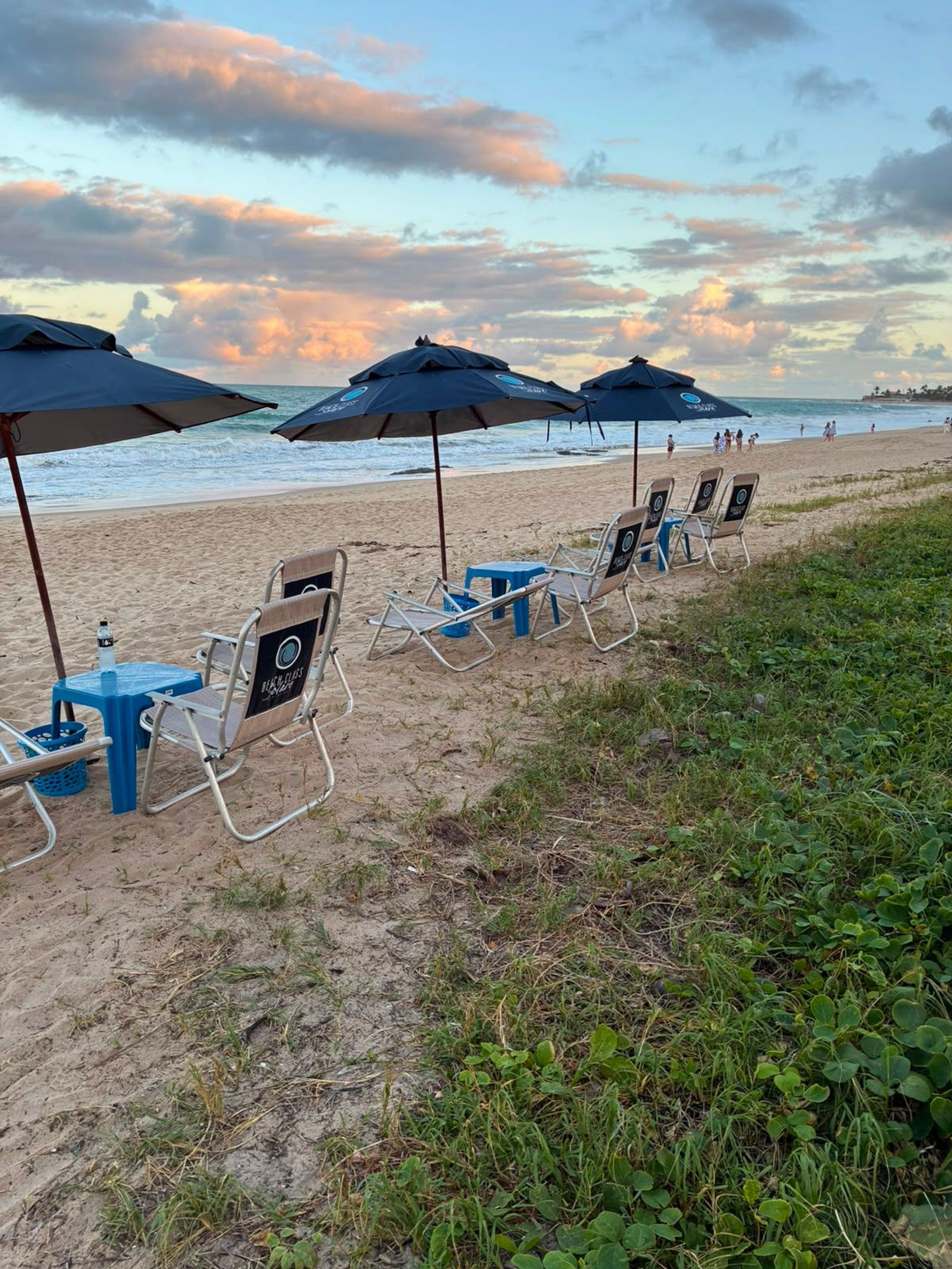 Cadeiras de praia e guarda-sóis dispostos na areia, com vista para o oceano e céu limpo.