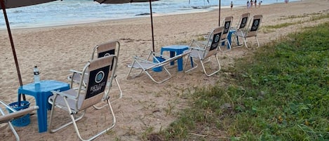 Beach chairs and umbrellas arranged on the sand, with a view of the ocean and a clear sky.