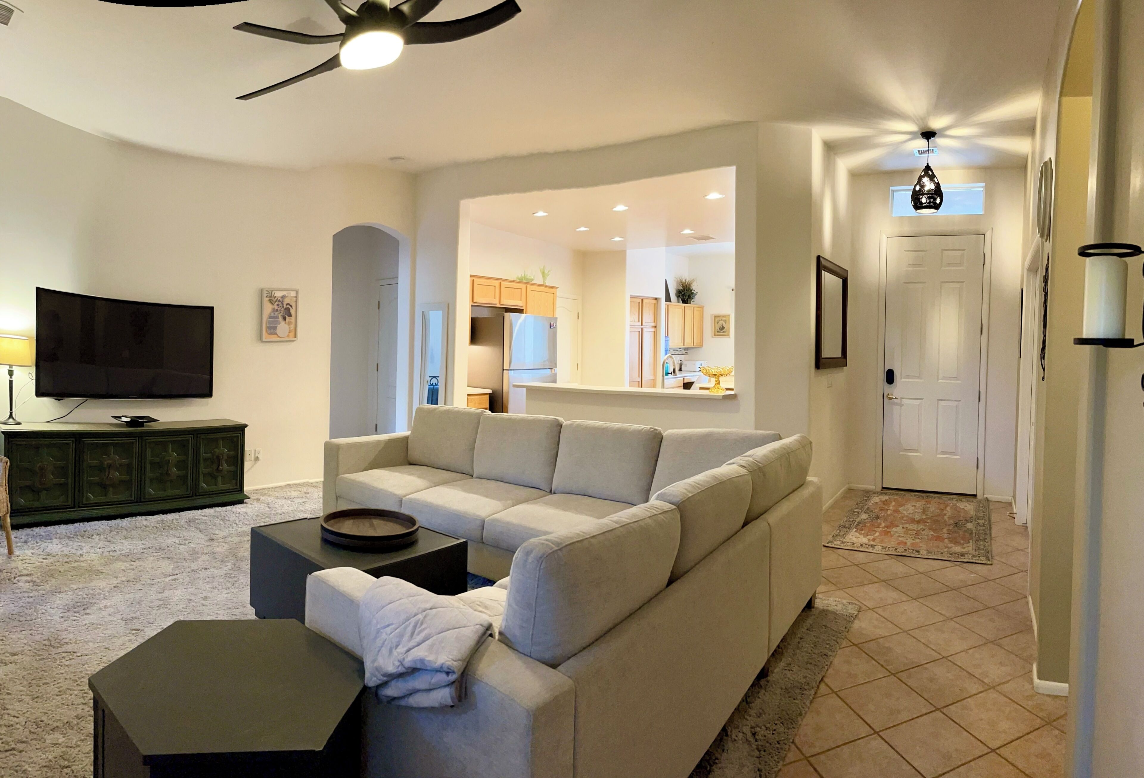 A living room with a sectional sofa, a television, and a ceiling fan.