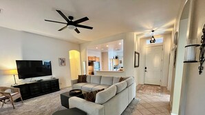 A living room with a flat-screen TV, a ceiling fan, a sofa, a coffee table, and a dining area visible in the background. - The Jewel near Sedona (Cornville)