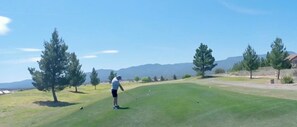 Eine Person auf einem Golfplatz, im Hintergrund Bäume und Berge.