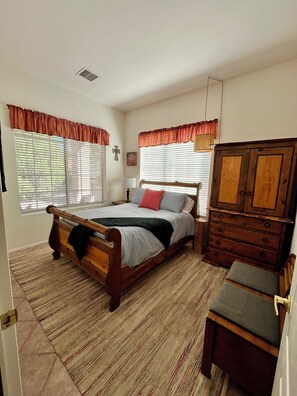 Quarto com cama de madeira, cômoda e janela com persianas.