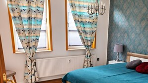 A bedroom with a bed, curtains, a nightstand, a lamp, and a floral-patterned rug.