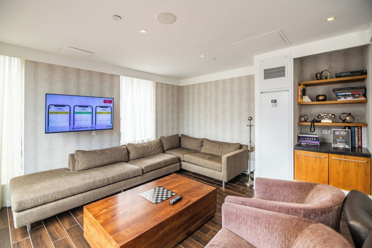 A modern living room with a sectional sofa, a wooden coffee table, a pink armchair, and a bookshelf with books and decorative items.
