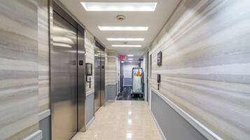 A hotel corridor with elevators, a trash bin, and a sign indicating an exit.
