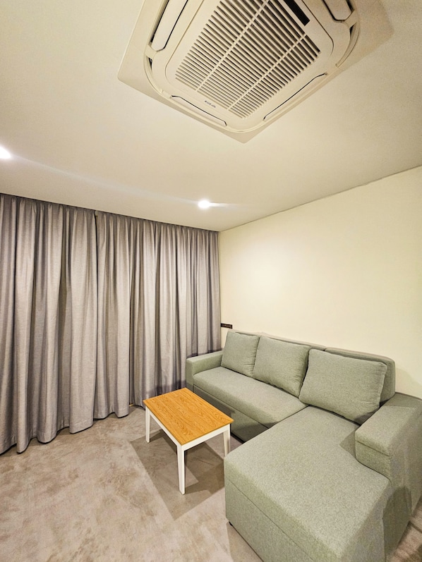 A living room with a grey sofa, a wooden coffee table, and a ceiling vent.