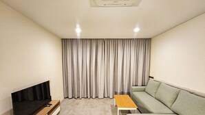 Ett modernt vardagsrum med en platt-TV, en soffa, ett soffbord och ett stort fönster med gardiner.