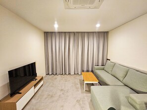 Ein modernes Wohnzimmer mit Flachbildfernseher, einer Couch, einem Couchtisch und einem großen Fenster mit Vorhängen.