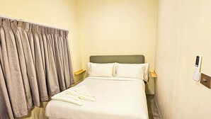 Ett hotellrum med en säng, gardiner, ett sängbord och ett vägguttag.