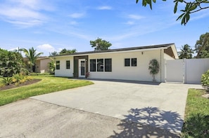 A single-story house with a front entrance, a driveway, and a small front yard with plants. - Spa Hot Tub | Mins to Beach | 2 Kings | Brand New! (Pompano Beach)