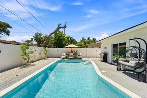 A rectangular swimming pool with a white border, surrounded by a white fence, and a hanging chair with cushions. - Spa Hot Tub | Mins to Beach | 2 Kings | Brand New! (Pompano Beach)
