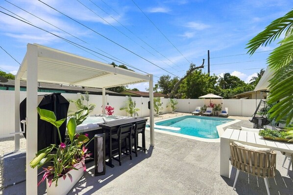 Ein Garten mit Swimmingpool, überdachter Terrasse und Sitzgelegenheit.