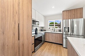A modern kitchen with wooden cabinets, stainless steel appliances, and a window with a view. - Spa Hot Tub | Mins to Beach | 2 Kings | Brand New! (Pompano Beach)