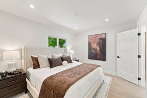 Ein modernes Schlafzimmer mit einem großen Bett, Nachttischen, einem Fenster und einer Tür.