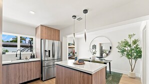 Une cuisine moderne avec des meubles en bois, des appareils en acier inoxydable, un îlot central et un coin repas agrémenté d’un grand miroir rond.