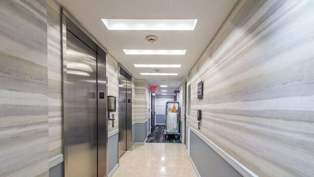 A hotel corridor with elevators, a trash bin, and a sign indicating an exit.