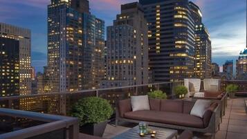 A rooftop terrace with outdoor seating, a city skyline in the background, and a prominent building with a spire.