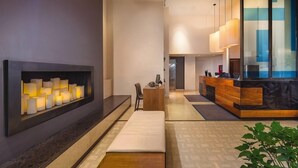 A modern hotel lobby with a reception desk, a seating area, and a wall-mounted light fixture.