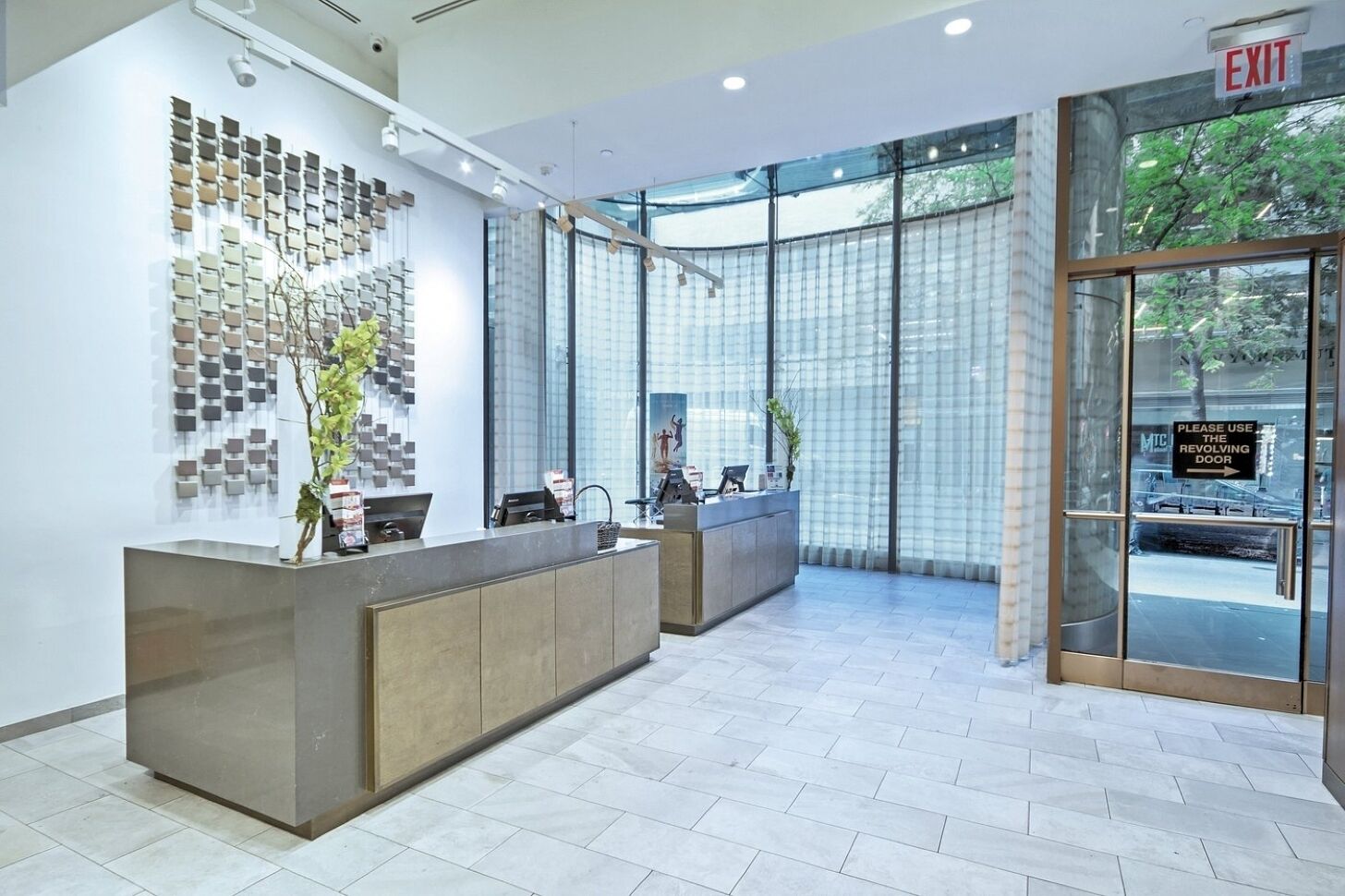 Un área de recepción con diseño moderno, que destaca por una gran pared de muestras de azulejos, un mostrador de recepción y un vidrio que da al exterior.