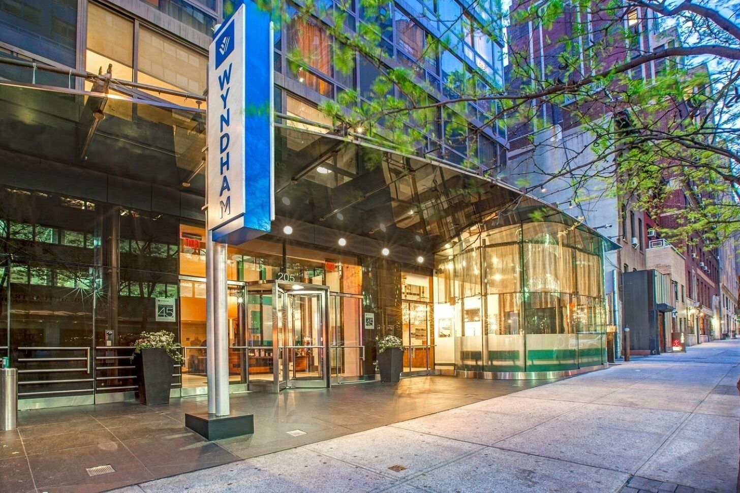 A modern hotel entrance with glass doors, a blue sign, and a clear view of the street.
