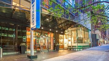 A modern hotel entrance with glass doors, a blue sign, and a clear view of the street.